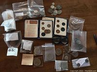 Overview of lot showing multiple resealable bags of coins and two sealed decimal coin sets on wooden surface