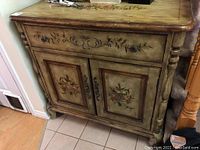 Full front view of the Lane cabinet showing the single drawer with floral decoration and two cupboard doors with painted fruit design, minor wear visible.