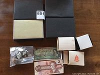 Four black coin cases (one open), loose coins in bag, one $1 bill, one $2 bill and small boxes