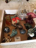 Box containing several assorted collectible items including glass figurines, paperweights, elephant figurines, rocks, and a ruby red glass jug.