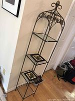 Full view of tall metal display stand with four square glass shelves and two framed tile trivets on lower shelves. Shows height and overall structure.
