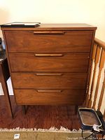 Front view of mid-century modern highboy dresser showing three drawers with carved wood handles and tapered legs on hardwood floor.
