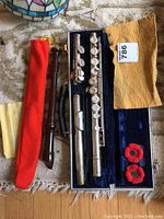 Flute pieces, recorder, polishing cloths, and case with red poppies visible on carpet.