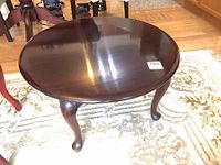 Angled full view of round table showing top and three cabriole legs.