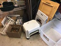 Overview of lot showing white plastic step stools, a box with glass jars, white and green plastic crates, and part of a black rubber mat.