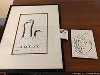 Two framed art prints side by side on a wooden surface, one by Benjamin Chee Chee showing three geese, the other by Doris Cyrette with abstract animal figures, with visible lot sticker.