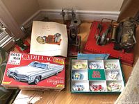 Overview photo showing 1968 Cadillac model kit box, Stirling Hot Air Engine manual and components, mechanical steam engine models, Red Rose tea mini teapots boxed set on floor.