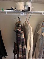 Tartan kilt, fisherman knit sweater, sporran, and belt hanging on a closet rack.