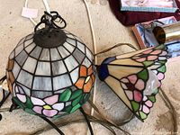 Pair of swag lamps with stained glass shades showing detailed floral and geometric designs and wiring with plugs.