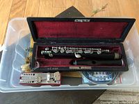 Piccolo flute in fitted case alongside metronome and measuring tape inside a plastic bin