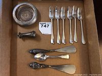 Complete lot in a box showing six forks, spoon, two shoe horns, salt shaker, and round coaster.