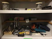 Shelf with power drills, drill bits in holders, metal hand planer, and small tools.