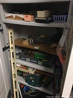 Shelving unit holding assorted tools including clamps, hand saw, small cases, and hardware.