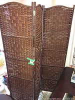 Three-panel dark brown woven wicker privacy screen, folding and standing upright, showing front face.