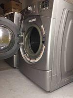 Front view of Whirlpool front load washer with door open showing stainless steel drum, minor surface scratches visible on side