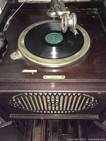 Close-up of phonograph turntable with record on spinning platform and metal tonearm positioned on record.