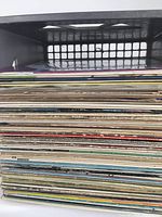 Side view of a stack of assorted vinyl LP records in sleeves showing the thickness and condition of the lot