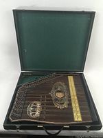 Full view of mandolin-zither seated in open hard case showing wood body, tuning pins, scale strip and felt-lined lid