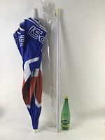Folded Pepsi beach umbrella with pole sections and Perrier bottle for scale