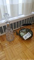 Photo of the Polish crystal decanter and metal kettle placed on wooden floor near a radiator and curtain.