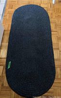 Oval dark gray braided area rug on a parquet floor, showing full length and shape.