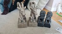 Two pairs of bookends: metallic rams with curved horns and carved Chinese lions in dark finish on a carpeted floor