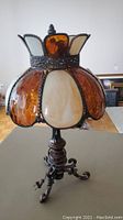 Full view of brass lamp with amber and cream glass shade on decorative brass base.