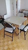 View of folding card table with four folding chairs around it on parquet floor
