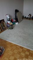 Wide image showing large beige carpet covering floor area with items around its edge