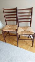 Pair of wooden ladder back chairs with woven wicker seats shown side by side.