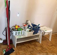 Photo showing broom, Swiffer mop, stick vacuum, two white plastic baskets with assorted cleaning supplies, blue cleaning bucket, white plastic shoe shelf