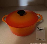Front view of the orange enameled cast iron pot with lid and black knob handle.
