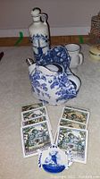 Photo showing Delft pottery jug, blue and white floral teapot, small white cup, and decorative coasters on the floor