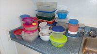 Wide assortment of plastic containers with lids in various sizes and colors stacked on a countertop corner.