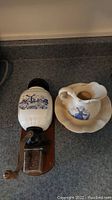 Wall-mounted ceramic coffee grinder with blue windmill design, wooden base, metal grinding mechanism, and hand crank with wooden handle next to a matching ceramic pitcher and bowl on the counter.