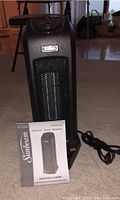 Sunbeam ceramic tower heater standing on carpet floor with instruction leaflet and power cord beside it