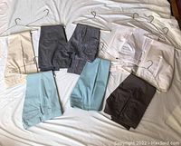 Photo of 7 pairs of women's pants in solid colors and patterns, laid on bed with hangers