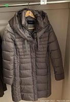 Small brown ladies puffer coat with hood and horizontal quilting hanging on wooden hanger