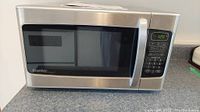 Front view of microwave showing stainless steel finish, door with handle, digital keypad, and timer display at 1:25.