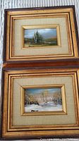 View of the two framed miniature landscape paintings stacked vertically, showing wood and gold-tone frames with beige textured mats.