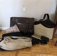 Lot of various purses and wallets arranged on the floor showing different sizes and styles including patterned, woven, beige and black items.
