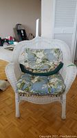 Front view of white rattan chair with floral cushions showing cushion pattern and chair design