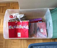Top-down view of a clear plastic storage bin containing gift bags and wrapping paper, with visible floral and solid prints.