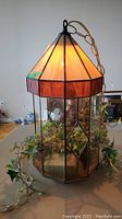 Front view of stained glass swag lamp illuminated with faux plant inside