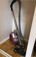 Side view of Dirt Devil Featherlite vacuum showing red canister, gray hose, metal wand, black floor nozzle.