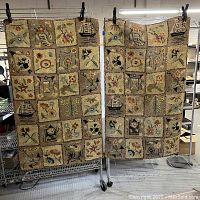 Photo of two rectangular area rugs hung side by side on racks, showing patchwork designs of floral and nautical motifs.