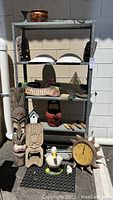 Overall view of garden collection items including tiki masks, pots, gardening tools, clock, and statues displayed on a metal shelf and ground.