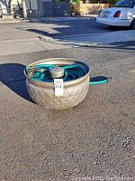 Photo of the garden hose coiled neatly inside the metal storage nest outdoors on pavement.