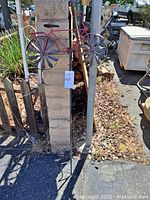 Metal bicycle sculpture mounted on a rod, with fan blade wheels and weathered red paint, shown outdoors against a cinder block wall and other yard items.