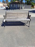 Front view of garden park bench showing six weathered wooden slats and cast iron sides with floral accents.